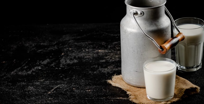 Rustic milk in a can and a glass on the table. On a black background. High quality photo